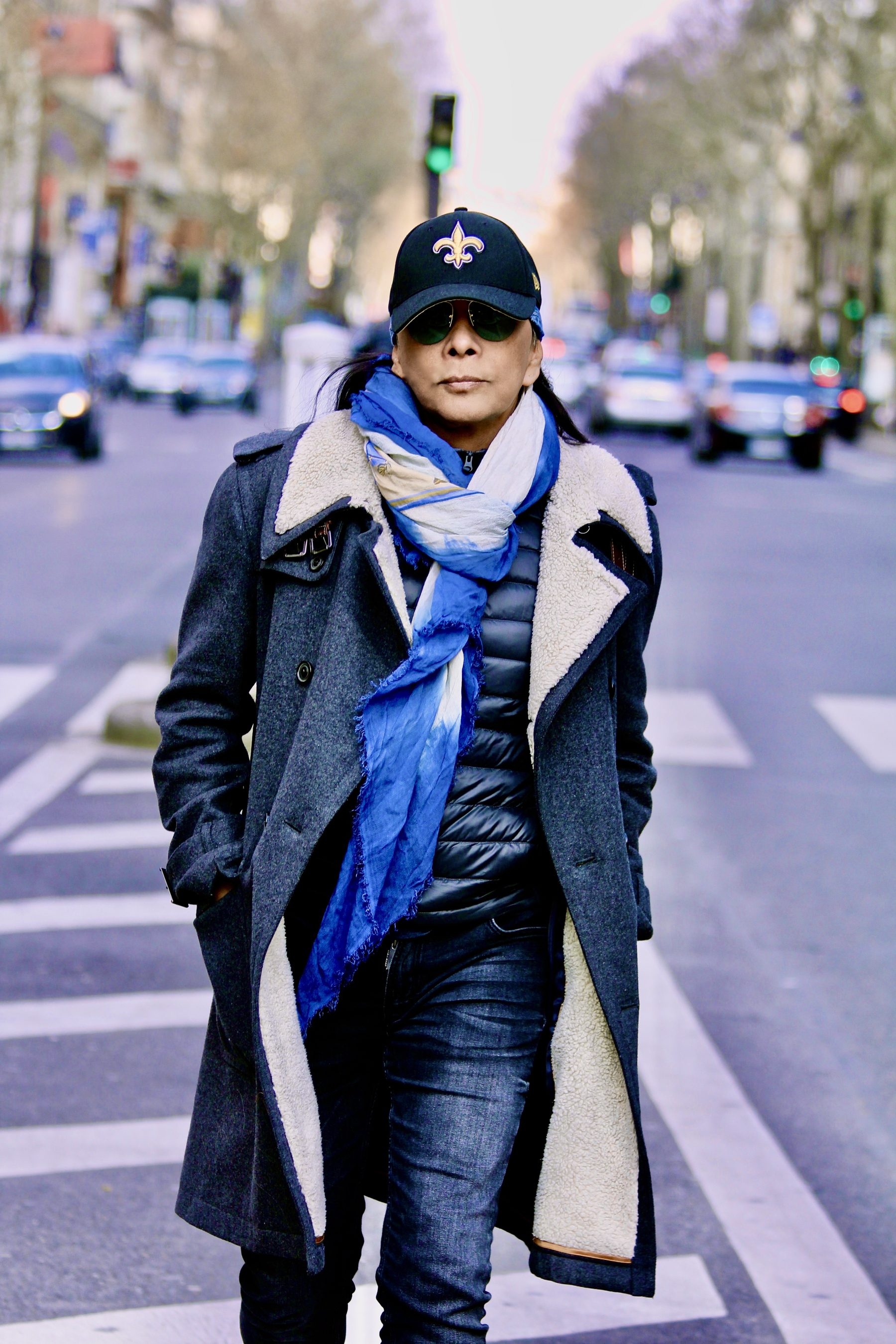 Dato Shake walking down a Paris boulevard in a grey coat and blue scarf